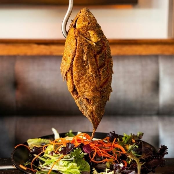 Crispy fried whole fish hanging over a fresh green salad with shredded carrots.