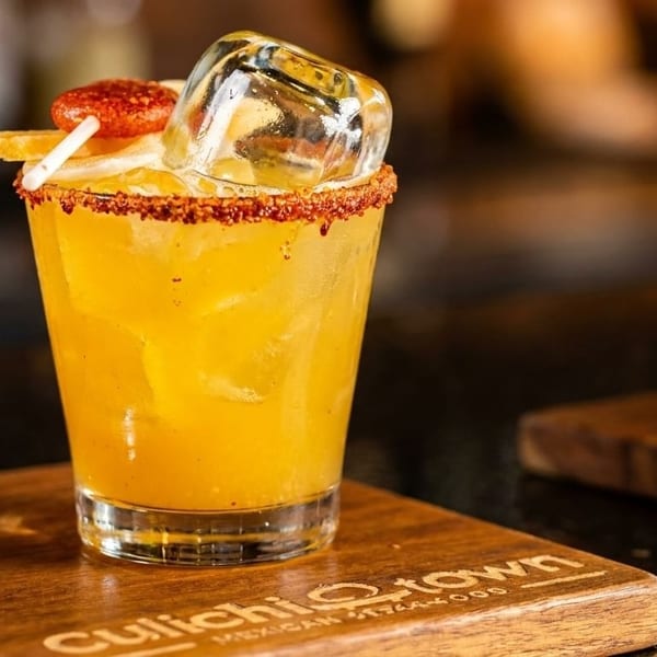 Two vibrant cocktails, one red and one yellow, garnished with spices and fruit on a wooden board.