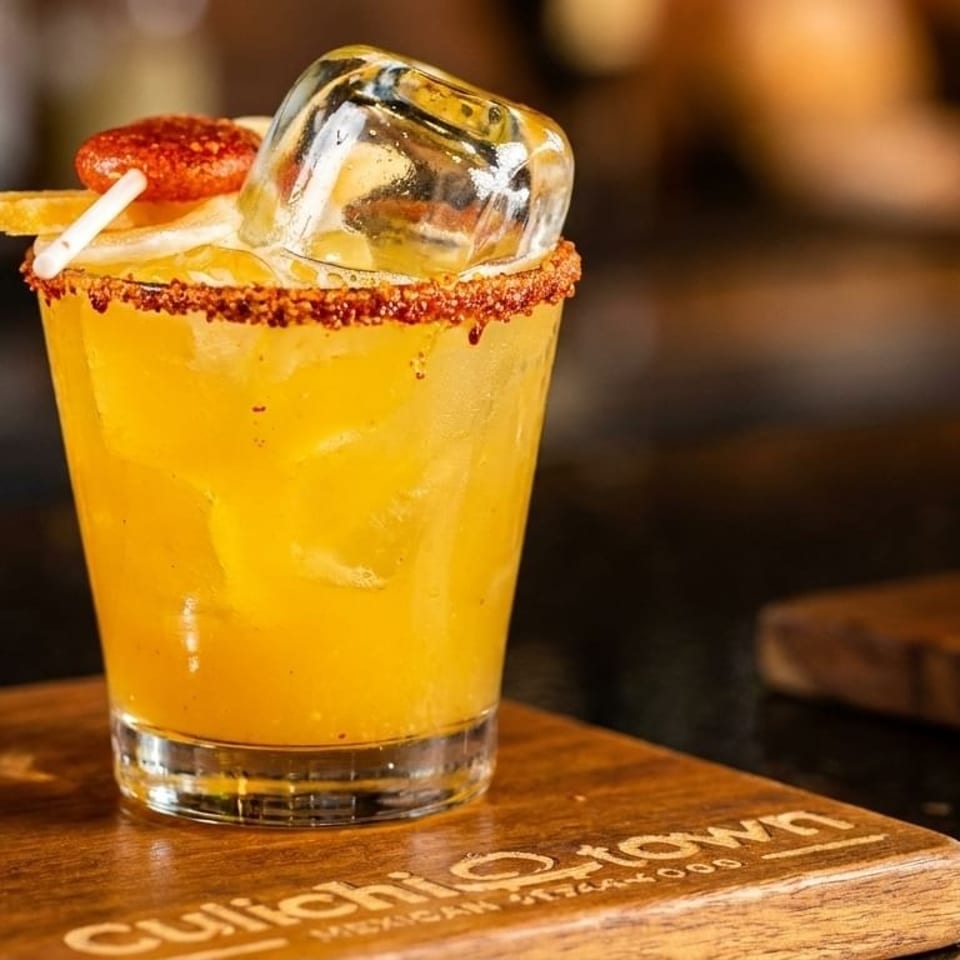 Two vibrant cocktails, one red and one yellow, garnished with spices and fruit on a wooden board.