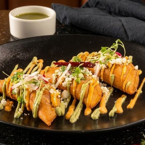 Crispy fried taquitos drizzled with green and orange sauces, topped with cheese, radishes, and herbs.