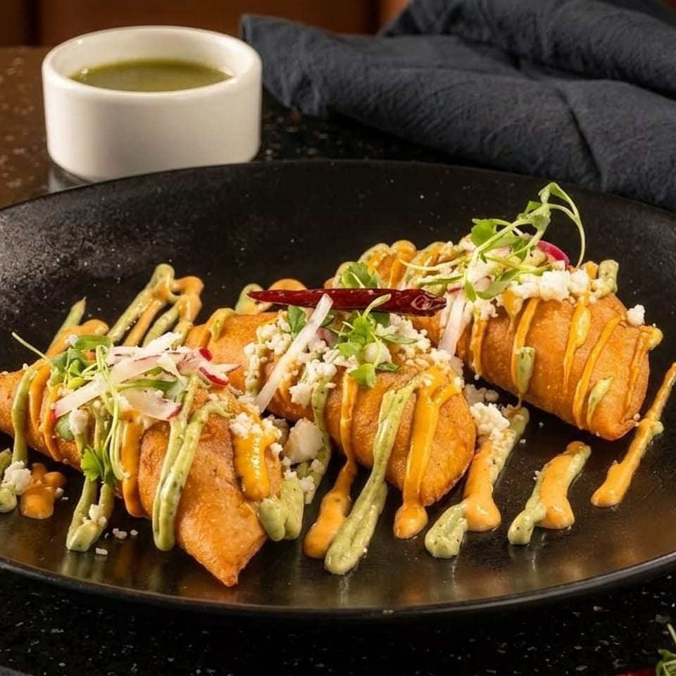 Crispy fried taquitos drizzled with green and orange sauces, topped with cheese, radishes, and herbs.