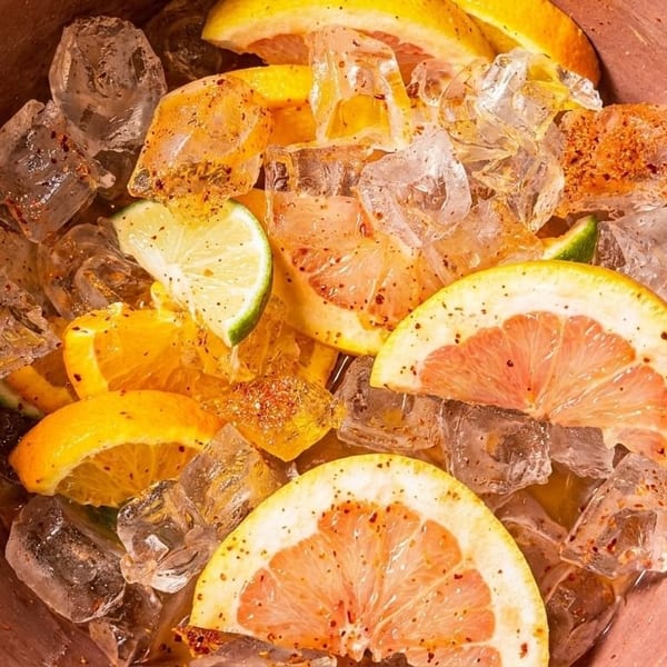 Close-up of a bowl filled with ice, orange slices, lime wedges, and grapefruit halves.