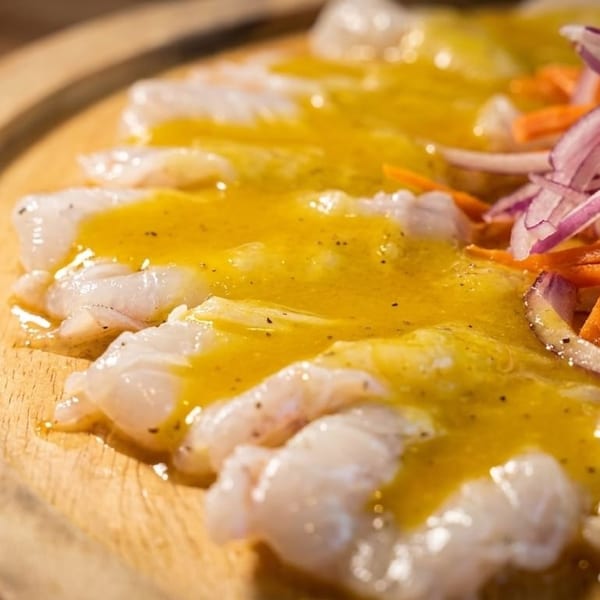 White fish ceviche with yellow sauce, julienned carrots, and red onions on a wooden plate.