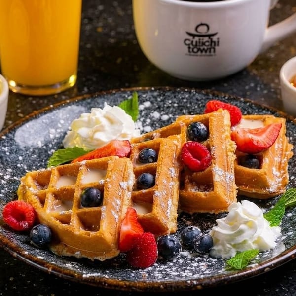 Golden waffles topped with berries, whipped cream, and powdered sugar, served with orange juice and coffee.