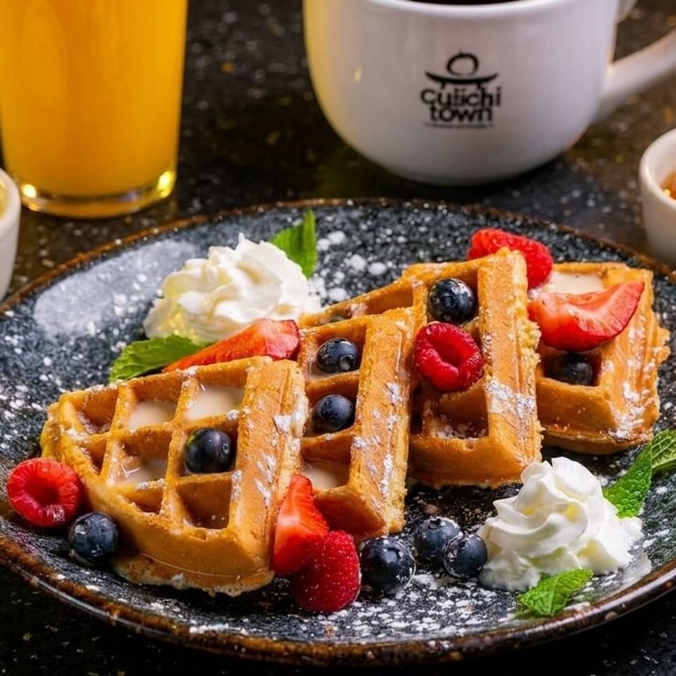 Golden waffles topped with berries, whipped cream, and powdered sugar, served with orange juice and coffee.