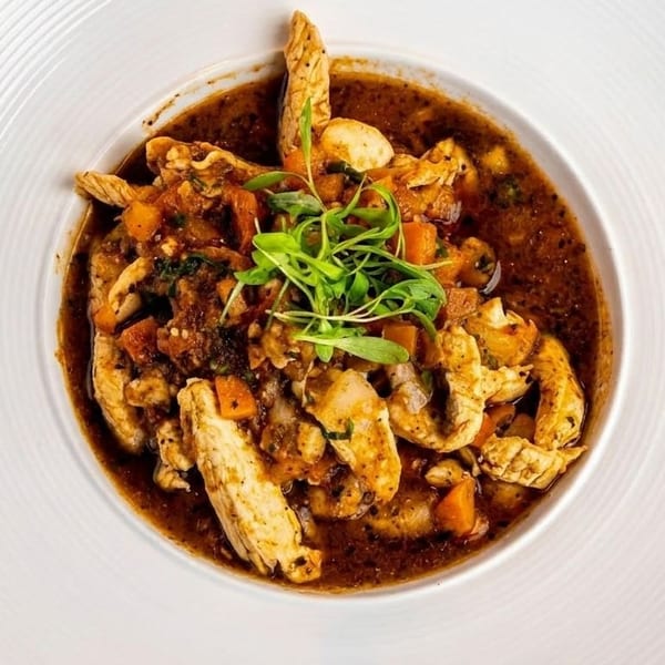 Chicken and vegetable stew in a rich brown sauce, garnished with fresh greens in a white bowl.