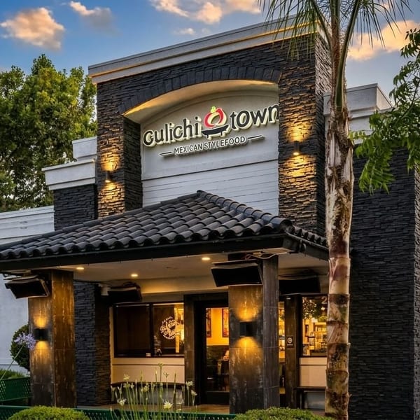 Exterior of Gulichi Town Mexican Style Food restaurant with stone facade, tiled roof entrance, and palm trees.