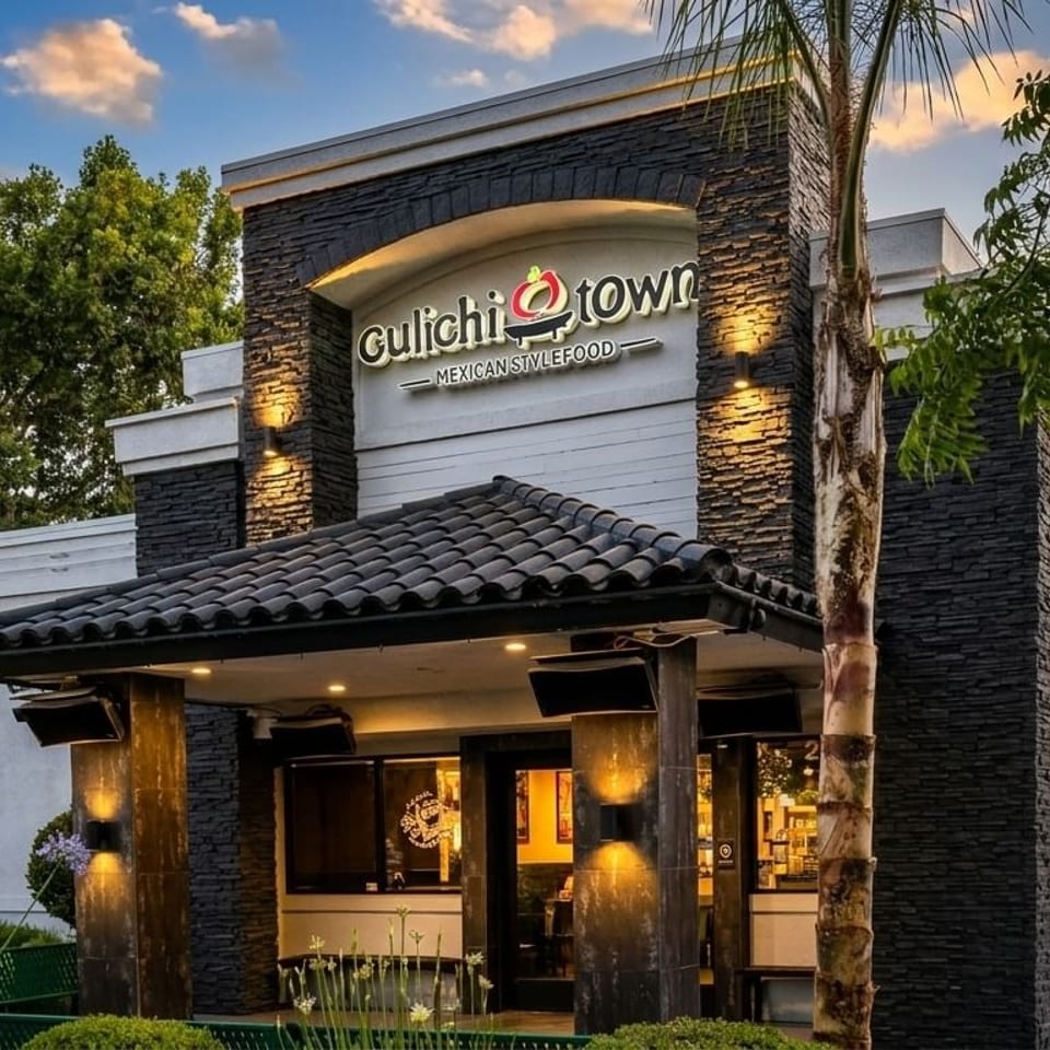 Exterior of Gulichi Town Mexican Style Food restaurant with stone facade, tiled roof entrance, and palm trees.