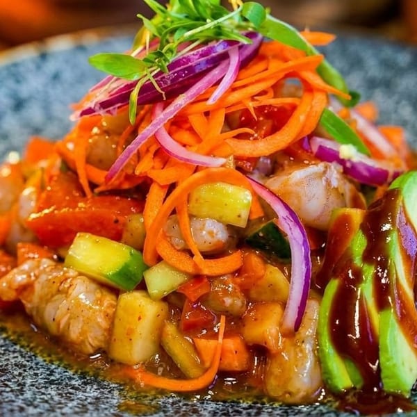 Shrimp ceviche with avocado, red onion, carrots, and cucumbers on a speckled gray plate.