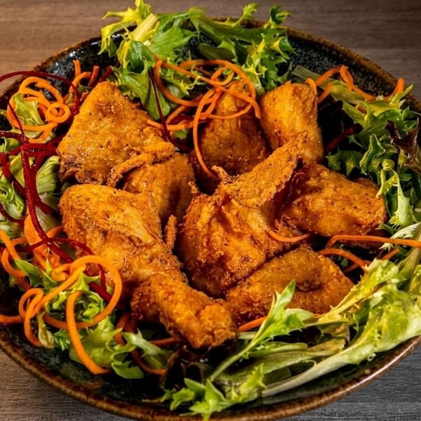 Crispy fried chicken pieces served on a bed of fresh green salad with shredded carrots and red beet.
