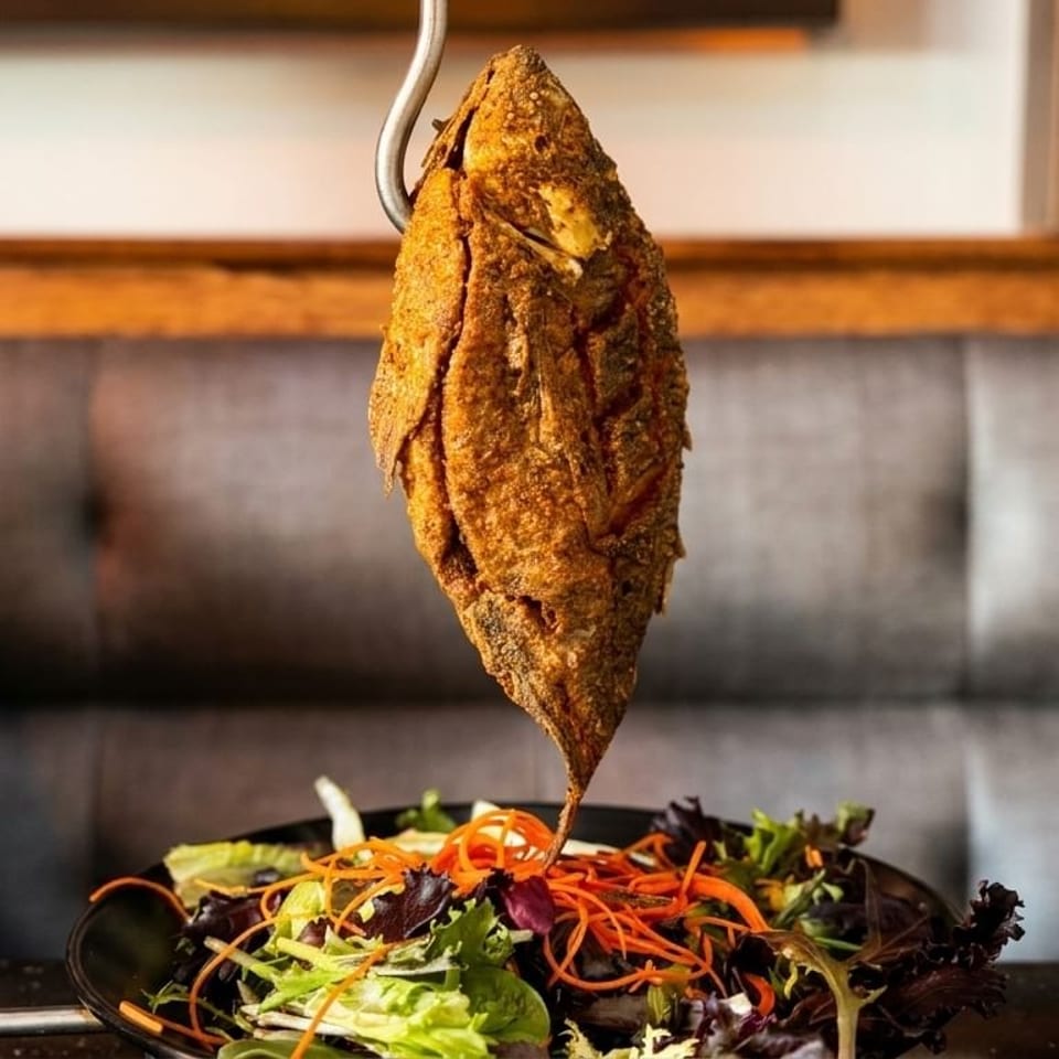 Crispy whole fried fish hanging over a fresh green salad with shredded carrots at a restaurant.